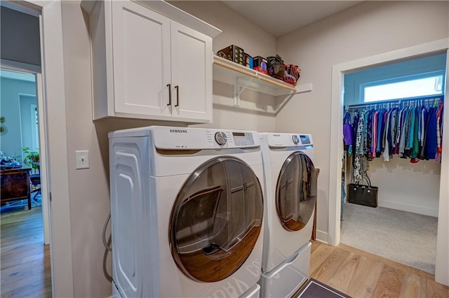 laundry area featuring washing machine and dryer, light wood finished floors, cabinet space, and baseboards