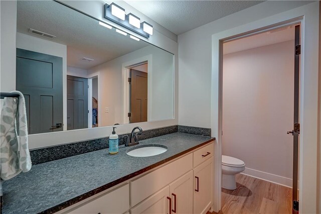 bathroom with wood finished floors, toilet, vanity, baseboards, and a textured ceiling