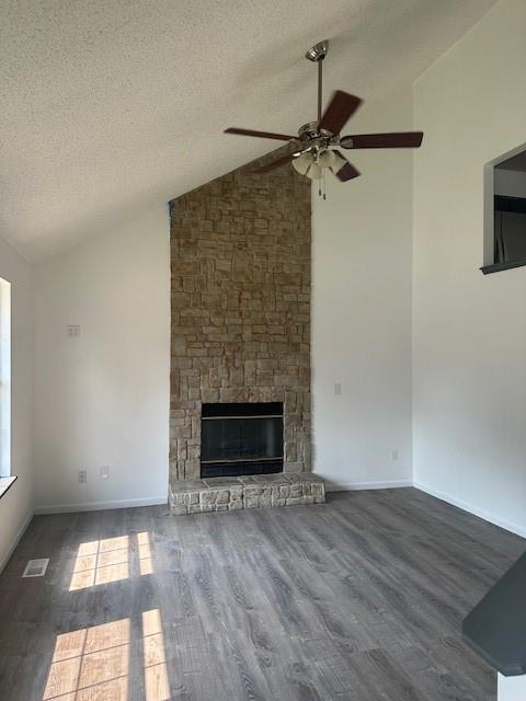 7037 N Holmes St, Gladstone, MO 64118 - unfurnished living room featuring a ceiling fan, wood finished floors, a textured ceiling, a stone fireplace, and baseboards