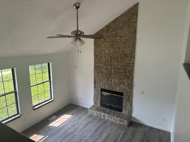 7037 N Holmes St, Gladstone, MO 64118 - unfurnished living room with wood finished floors, a ceiling fan, lofted ceiling, a stone fireplace, and a textured ceiling