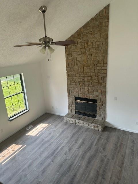 7037 N Holmes St, Gladstone, MO 64118 - unfurnished living room featuring lofted ceiling, ceiling fan, wood finished floors, a stone fireplace, and a textured ceiling
