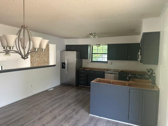 7037 N Holmes St, Gladstone, MO 64118 - kitchen featuring stainless steel appliances, a textured ceiling, wood finished floors, a chandelier, and a peninsula