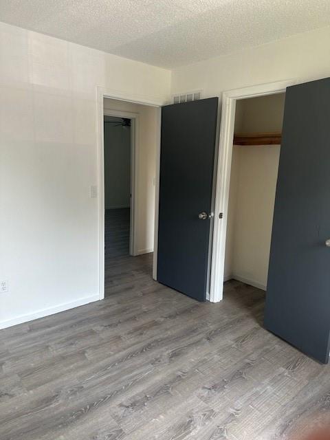 7037 N Holmes St, Gladstone, MO 64118 - unfurnished bedroom with a closet, wood finished floors, a textured ceiling, and baseboards