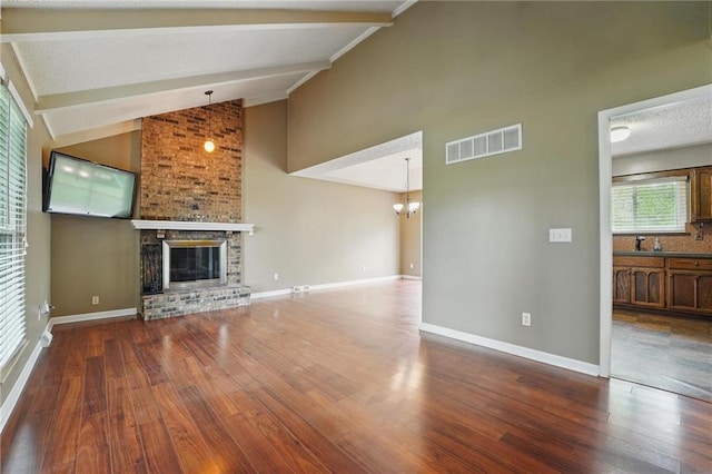 unfurnished living room with wood finished floors, a brick fireplace, beam ceiling, a chandelier, and baseboards