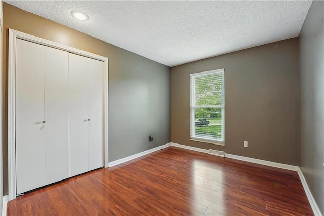 unfurnished bedroom with wood finished floors, a textured ceiling, baseboards, and a closet