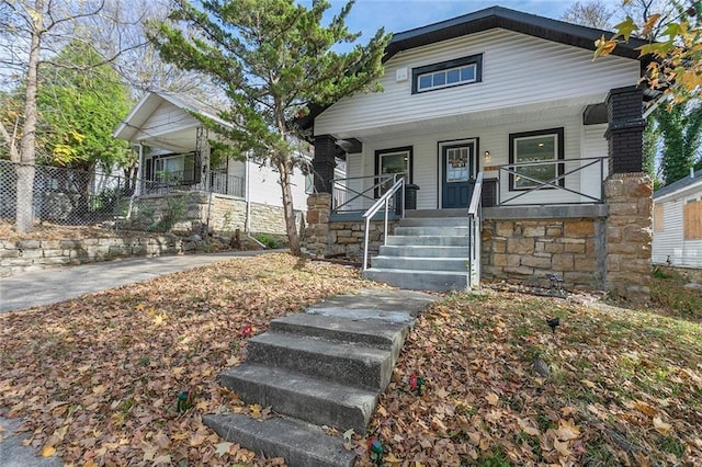 shotgun-style home featuring covered porch, stairs, stone siding, and fence