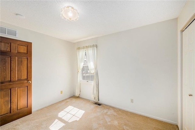 unfurnished bedroom featuring light colored carpet, a textured ceiling, and baseboards