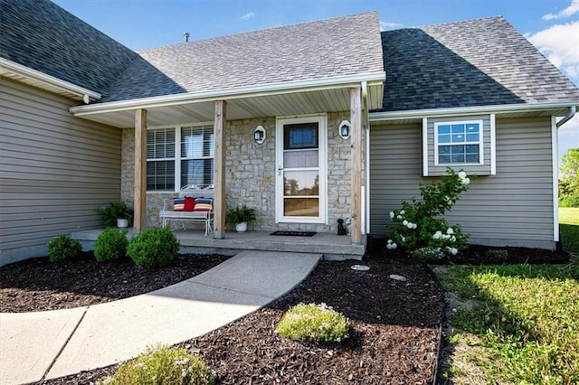 entrance to property featuring covered porch, a shingled roof, and stone siding