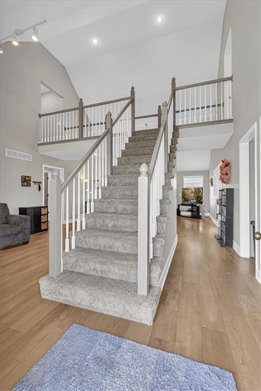 stairs with high vaulted ceiling, wood finished floors, and recessed lighting