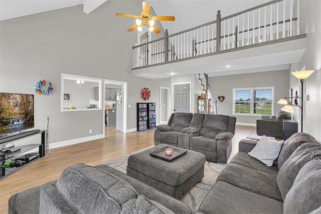 living room featuring high vaulted ceiling, ceiling fan, baseboards, wood finished floors, and beam ceiling