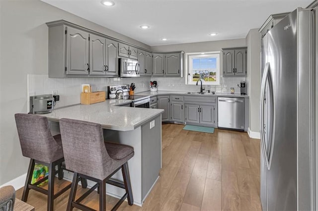 kitchen featuring appliances with stainless steel finishes, gray cabinetry, a peninsula, a sink, and recessed lighting