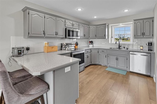 kitchen featuring appliances with stainless steel finishes, gray cabinetry, a sink, a peninsula, and a kitchen breakfast bar