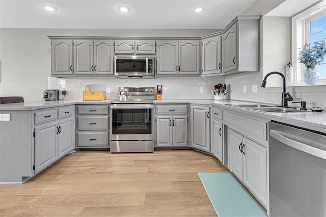 kitchen featuring appliances with stainless steel finishes, gray cabinetry, a peninsula, a sink, and backsplash