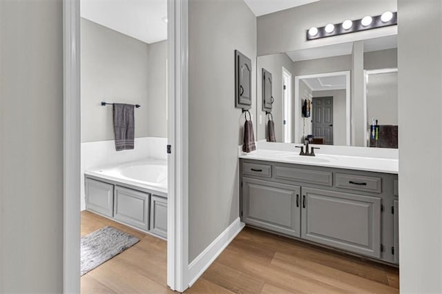 bathroom with wood finished floors, vanity, a bath, and baseboards