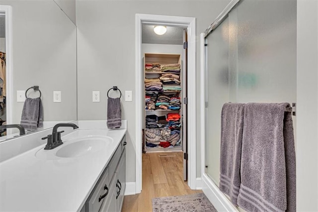 bathroom featuring a shower stall, a walk in closet, vanity, wood finished floors, and baseboards