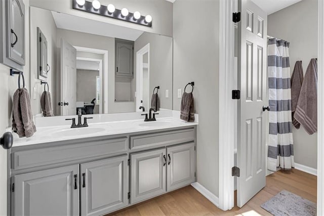 bathroom with wood finished floors, double vanity, baseboards, and ensuite bath