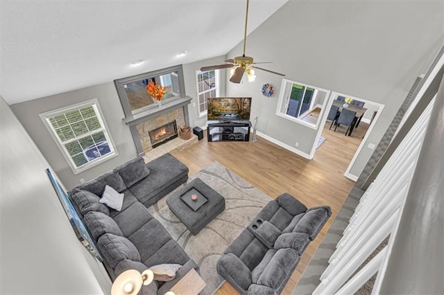 living area featuring wood finished floors, a stone fireplace, lofted ceiling, baseboards, and a ceiling fan