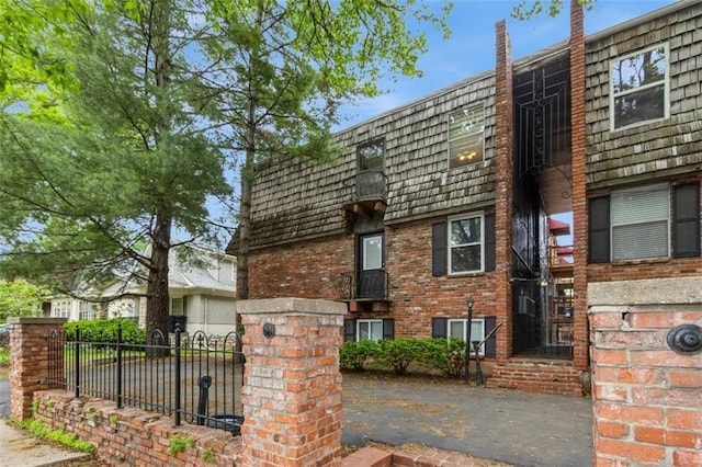 view of front facade featuring mansard roof, fence, and brick siding