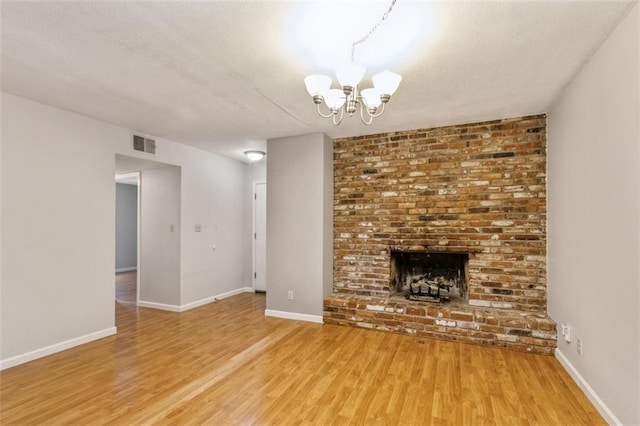 unfurnished living room featuring light wood-type flooring, a chandelier, a brick fireplace, baseboards, and a textured ceiling