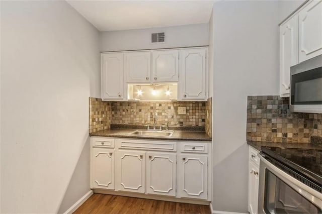 kitchen with dark countertops, appliances with stainless steel finishes, a sink, white cabinetry, and wood finished floors