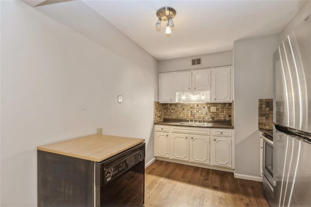 kitchen featuring freestanding refrigerator, a sink, tasteful backsplash, wood finished floors, and dark countertops