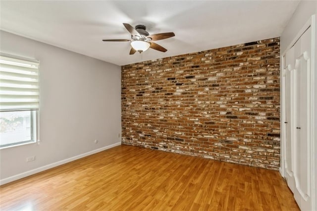unfurnished room with brick wall, a ceiling fan, light wood finished floors, and baseboards