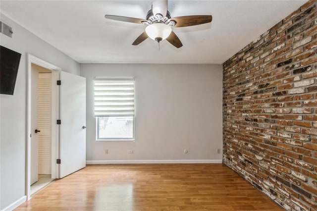 unfurnished bedroom with wood finished floors, baseboards, and brick wall