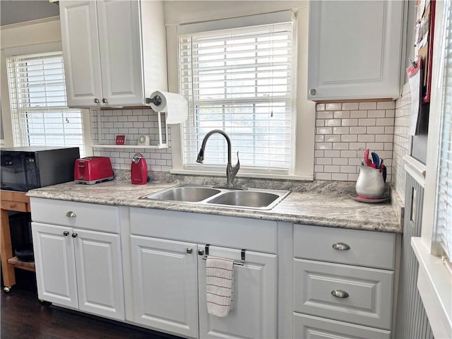 kitchen with black microwave, a sink, white cabinets, and decorative backsplash