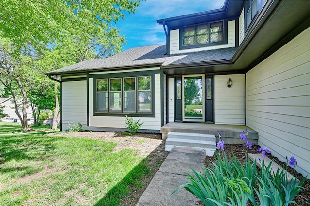 view of exterior entry with a yard and roof with shingles