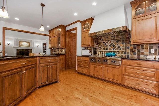 7711 N Montgall Ave, Kansas City, MO 64119 - kitchen featuring custom range hood, stainless steel gas stovetop, decorative backsplash, a fireplace, and light wood-style floors
