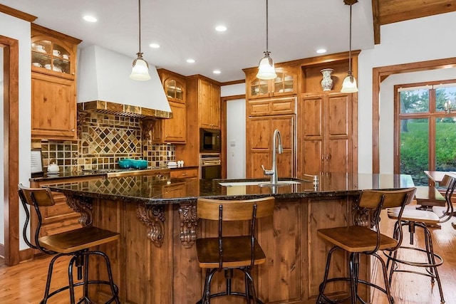 7711 N Montgall Ave, Kansas City, MO 64119 - kitchen with stainless steel oven, light wood-style flooring, custom range hood, black microwave, and tasteful backsplash