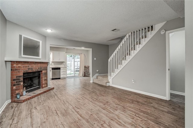 5516 66th Ter, Kansas City, MO 64151 - unfurnished living room featuring a textured ceiling, wood finished floors, stairway, a brick fireplace, and baseboards