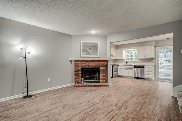 5516 66th Ter, Kansas City, MO 64151 - unfurnished living room featuring light wood finished floors, a fireplace, a textured ceiling, baseboards, and a sink