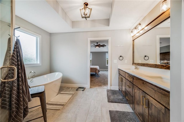 bathroom with connected bathroom, a freestanding tub, double vanity, baseboards, and a tray ceiling