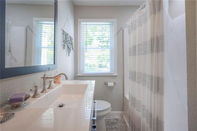 full bath featuring toilet, vanity, a textured wall, baseboards, and shower / bath combo