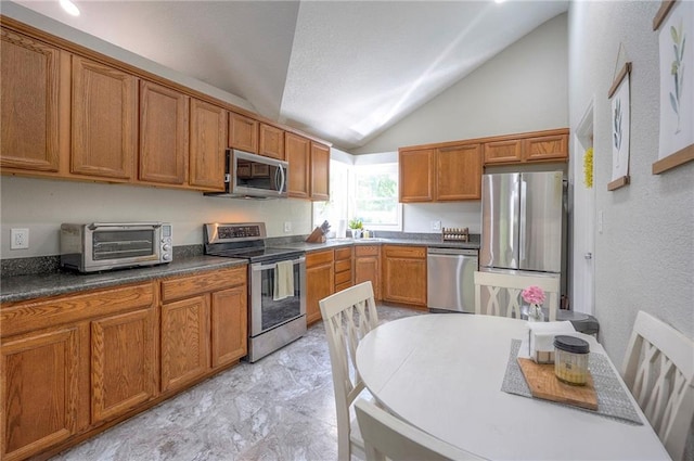kitchen with appliances with stainless steel finishes, lofted ceiling, brown cabinetry, dark countertops, and a sink