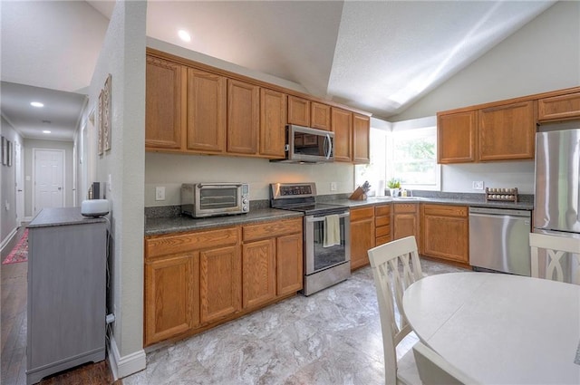 kitchen featuring stainless steel appliances, vaulted ceiling, brown cabinets, and dark countertops