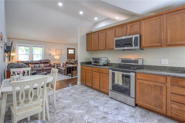 kitchen with appliances with stainless steel finishes, brown cabinets, dark countertops, lofted ceiling, and open floor plan