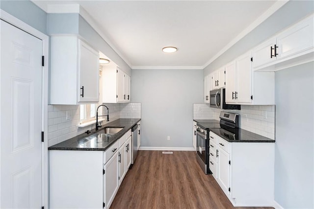 kitchen with appliances with stainless steel finishes, a sink, white cabinetry, dark wood-style flooring, and backsplash
