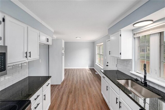 kitchen with a sink, wood finished floors, dark stone counters, and white cabinets