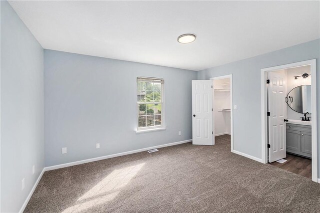 unfurnished bedroom with dark colored carpet, baseboards, a walk in closet, ensuite bath, and a closet