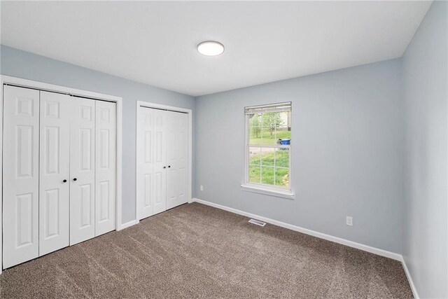unfurnished bedroom featuring carpet flooring, two closets, and baseboards