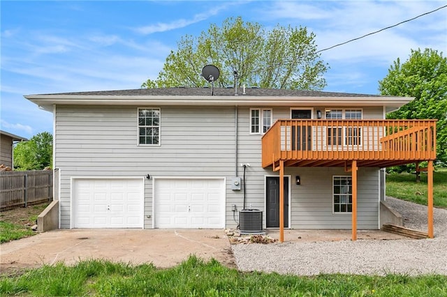 rear view of property with an attached garage, a wooden deck, concrete driveway, fence, and cooling unit