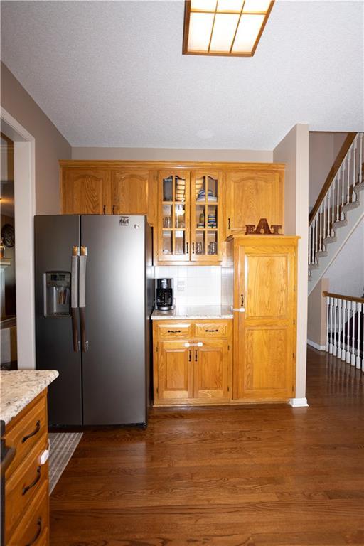 16366 S Hunter St, Olathe, KS 66062 - kitchen with fridge with ice dispenser, dark wood-style floors, glass insert cabinets, and brown cabinets