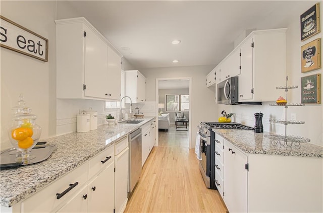 4547 Wyoming St, Kansas City, MO 64111 - kitchen featuring appliances with stainless steel finishes, a sink, light wood finished floors, white cabinets, and recessed lighting