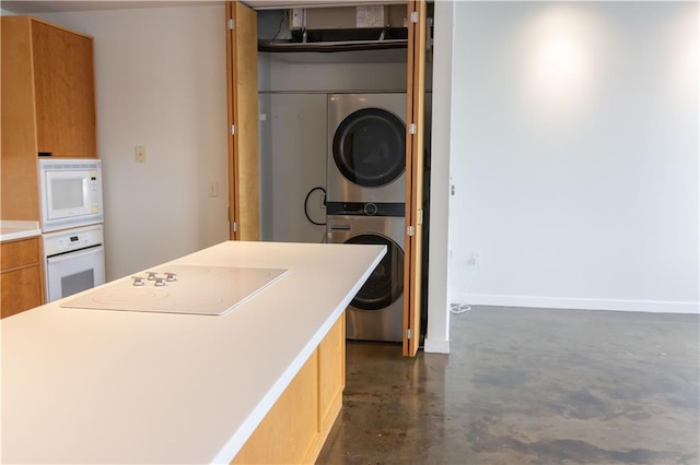 kitchen featuring white appliances, stacked washing machine and dryer, concrete flooring, light countertops, and baseboards