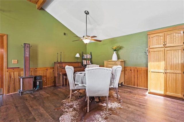 dining room with wainscoting, wood walls, wood finished floors, a wood stove, and ceiling fan