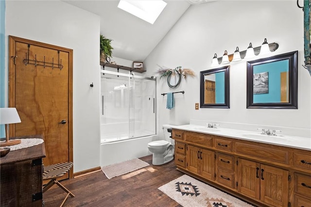 bathroom featuring a skylight, lofted ceiling, wood finished floors, combined bath / shower with glass door, and double vanity