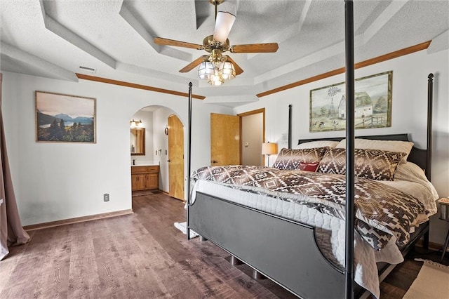 bedroom featuring a raised ceiling, arched walkways, wood finished floors, a textured ceiling, and ensuite bath