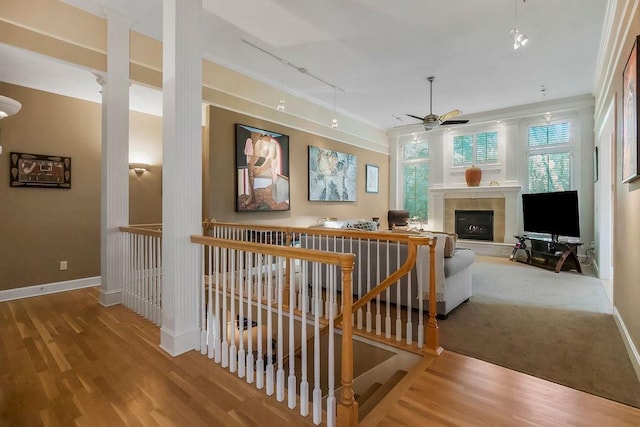 corridor with rail lighting, wood finished floors, an upstairs landing, and baseboards